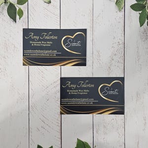 May include: Two black business cards with gold lettering and a gold heart logo. The text on the cards reads "Amy Tollerton", "Homemade Wax Melts & Home Fragrance", "scentdownthelane@gmail.com", and "www.scentdownthelane.co.uk". The logo is a gold heart with the word "Scent" inside.
