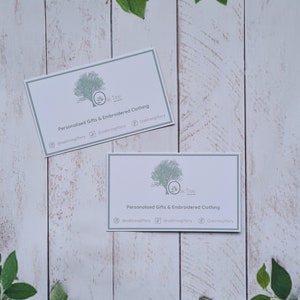 May include: Two white business cards with a green tree logo and the text "Oak Tree" and "Personalized Gifts & Embroidered Clothing" on a white wood background.
