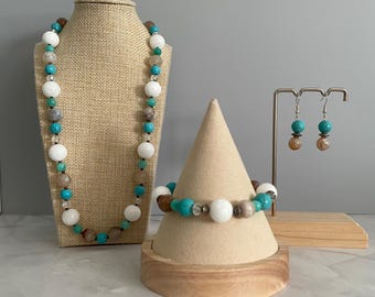 May include: A jewelry set consisting of a beaded necklace, a beaded bracelet, and a pair of drop earrings. The pieces feature a repeating pattern of white, turquoise, and brown spherical beads accented with small clear and metallic spacers.