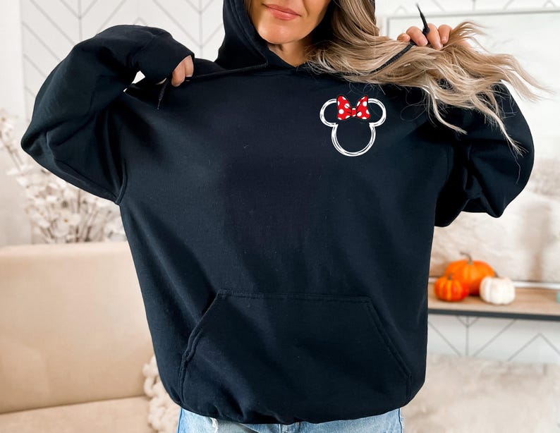 May include: Black hooded sweatshirt with a white outline of a cartoon mouse head with a red bow. The bow has white polka dots.
