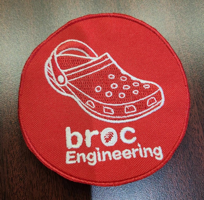 K&ouml;nnte beinhalten: Roter gestickter Aufn&auml;her mit einer wei&szlig;en Umrandung eines Clogs und dem Text "broc Engineering" in wei&szlig;.