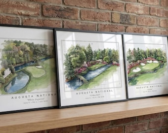 May include: Three framed watercolor prints of Augusta National golf course holes. Each print features a different hole with a detailed illustration of the course layout, trees, and water features. The frames are black, and the prints are displayed on a wooden shelf.