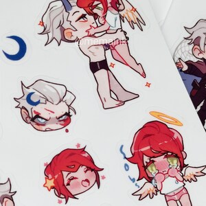 May include: A sheet of stickers with anime-style illustrations. The stickers show characters with red and white hair, wings, halos, and horns. Some characters are embracing, while others have emotional expressions.