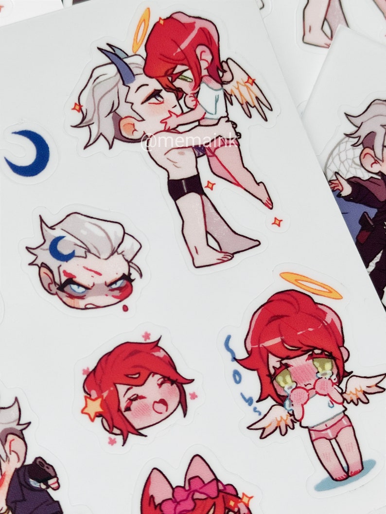 May include: A sheet of stickers with anime-style illustrations. The stickers show characters with red and white hair, wings, halos, and horns. Some characters are embracing, while others have emotional expressions.