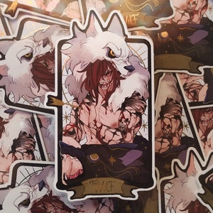 Puede incluir: Una pegatina con una criatura sangrienta con forma de lobo, con pelo rojo y una capucha de piel de lobo blanca. La criatura sostiene un cuchillo ensangrentado y tiene una expresión feroz. La pegatina tiene un borde dorado y el texto "The Wolf" en una pancarta en la parte inferior.