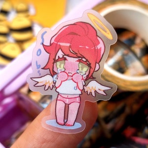 May include: A transparent sticker of a crying angel character with red hair, a gold halo, and small white wings. The angel is wearing a white top and pink underwear. The sticker has the text "sob boss" on the side.