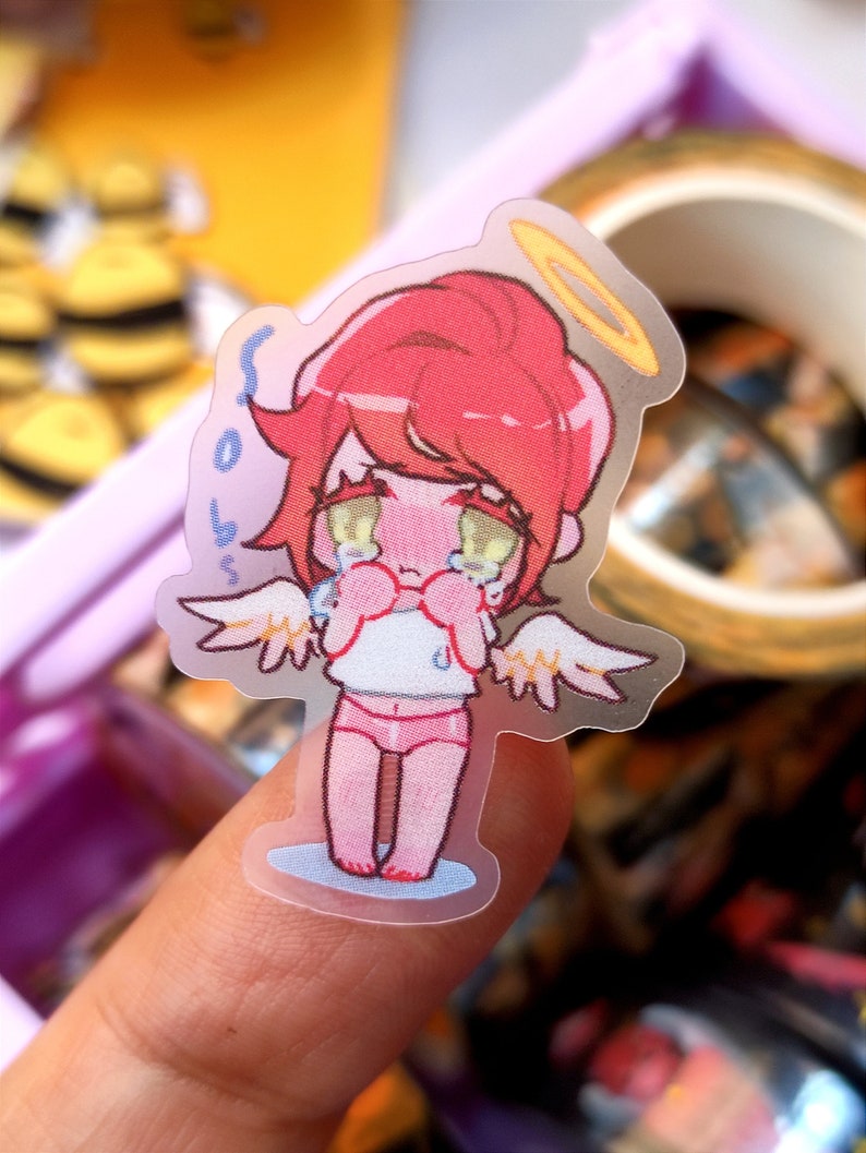 May include: A transparent sticker of a crying angel character with red hair, a gold halo, and small white wings. The angel is wearing a white top and pink underwear. The sticker has the text "sob boss" on the side.