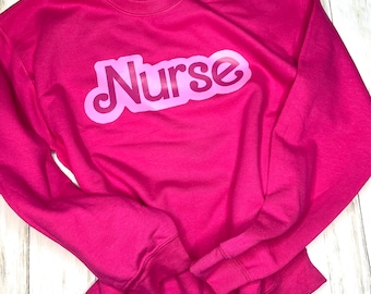 May include: A pink sweatshirt with the word "Nurse" printed in a large, pink, retro-style font.