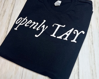 May include: Black t-shirt with the text "openly GAY" printed in white.