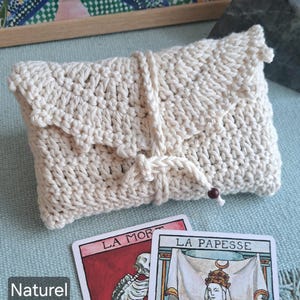 May include: A cream-coloured, hand-crocheted clutch bag with a flap closure and knotted cord detail. Two tarot cards, "La Mort" and "La Papesse", are visible. The word "Naturel" is printed on the left side of the image.