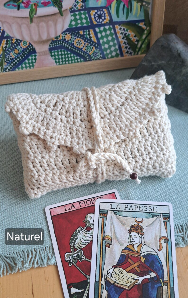 May include: A cream-coloured, hand-crocheted clutch bag with a flap closure and knotted cord detail. Two tarot cards, "La Mort" and "La Papesse", are visible. The word "Naturel" is printed on the left side of the image.