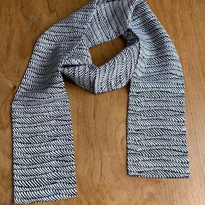 May include: A black and white patterned scarf with a wavy design. The scarf is made of a soft, lightweight fabric and is perfect for adding a touch of style to any outfit.