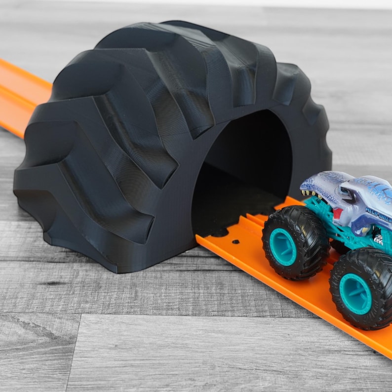 Peut inclure: Un tunnel en forme de pneu de camion monstre noir imprim&eacute; en 3D avec une piste orange. Un jouet de camion monstre avec des accents bleus et turquoise est positionn&eacute; sur la piste. Un jouet amusant pour les enfants.