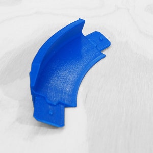Puede incluir: Una pieza de esquina de plástico azul para una pista o un conjunto de juguetes. La pieza es curva y tiene una superficie lisa.