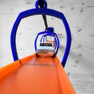 May include: A white toy car drives on an orange track through a series of blue plastic loops.
