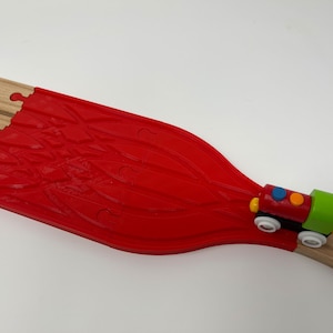 May include: A red wooden train track with a toy train on it. The train is red, green, and blue with white wheels. The train is going around a curve in the track.