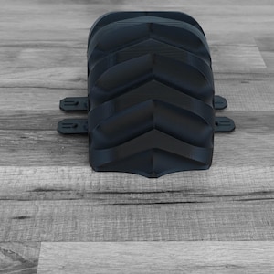 Peut inclure: Un objet noir incurv&eacute; et textur&eacute; avec une s&eacute;rie de cr&ecirc;tes en forme de chevrons. Deux petites languettes rectangulaires s'&eacute;tendent des c&ocirc;t&eacute;s. L'objet est pos&eacute; sur une surface en bois grise.