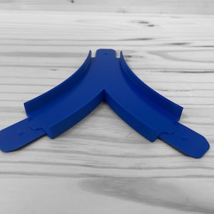 Puede incluir: Una pieza de pista de plástico azul para una pista de carreras de coches de juguete. La pieza tiene forma de Y y tiene dos ranuras en cada extremo para conectar con otras piezas de pista.