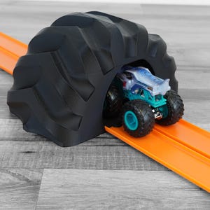 May include: A black, tyre-shaped tunnel with an orange race track guides a teal and blue monster truck. The toy truck has large black tyres with teal rims. The tunnel is a 3D-printed design.