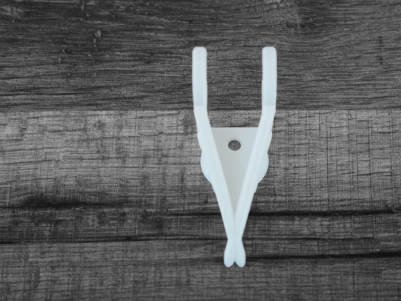 Puede incluir: Un colgador de guitarra blanco, impreso en 3D, para montar en la pared. El colgador presenta un dise&ntilde;o &uacute;nico con dos brazos curvos y un soporte central con un agujero. El dise&ntilde;o recuerda a alas. El colgador est&aacute; dise&ntilde;ado para sujetar una guitarra.