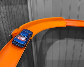 May include: A blue toy car races down an orange plastic track.