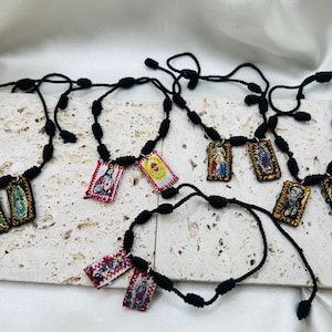 May include: Five black cord necklaces with religious medallions. Each necklace has a different image of a saint or religious figure. The medallions are colorful and feature gold accents.