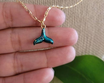 May include: A gold chain necklace with a green and blue enamel mermaid tail pendant. The tail has a sparkly finish.