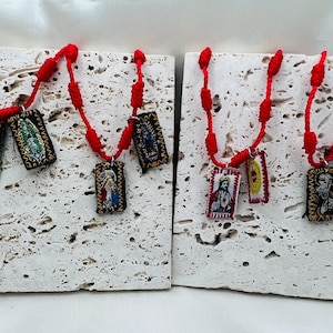 May include: Two red string necklaces with religious medallions. The medallions feature images of saints and the Virgin Mary.
