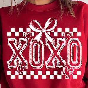 Puede incluir: Sudadera roja con un patr&oacute;n de cuadros blancos, un lazo blanco y la palabra "XOXO" en blanco con corazones.