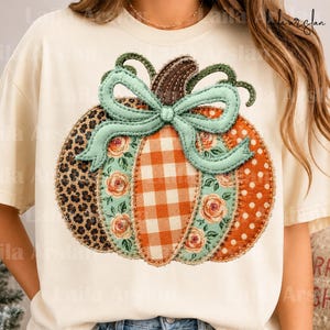 May include: A cream-colored t-shirt featuring a large pumpkin graphic. The pumpkin is divided into vertical sections with different patterns: leopard print, floral print, orange gingham, and orange with white polka dots, topped with a teal bow.