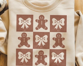 Puede incluir: Una sudadera beige con un diseño marrón y blanco de hombres de jengibre y lazos. El diseño está en un patrón de tablero de ajedrez.