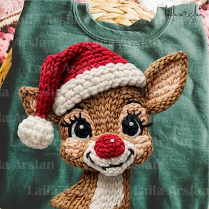 Può includere: Una felpa verde con un volto di renna lavorato a maglia con un cappello da Babbo Natale rosso. La renna ha la pelliccia marrone, un naso rosso e grandi occhi. Il cappello ha un bordo bianco e un pompon bianco.