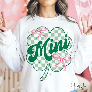 May include: White sweatshirt with a green shamrock design and the word "Mini" in a retro font. The shamrock has a checkered pattern and pink bows.