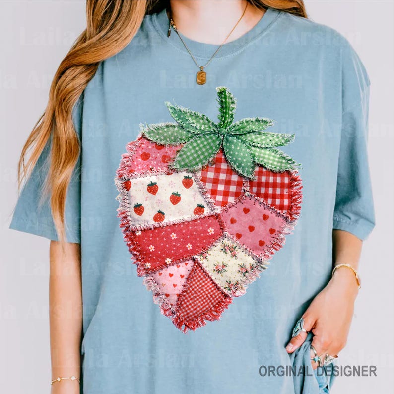 May include: Light blue t-shirt featuring a patchwork strawberry design. The strawberry is composed of various fabric patterns, including gingham, floral, and polka dots, in shades of red, pink, and white. The shirt has short sleeves and a crew neck.
