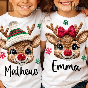 Könnte beinhalten: Zwei weiße T-Shirts mit Rentiergesichtern und Namen. Ein Rentier hat einen grün-weißen Hut, das andere eine rote Schleife. Beide haben braune Geweihe, rote Nasen und schwarze Augen. Der Name "Matheue" steht auf einem Shirt und "Emma" auf dem anderen.