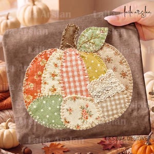May include: A brown fabric square featuring a central pumpkin applique made from various patterned fabric patches including orange floral, beige gingham, green polka dot, and cream floral prints, accented with a white lace piece and brown stem.