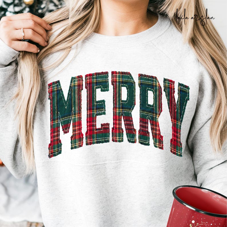 Puede incluir: Una sudadera gris claro de cuello redondo con la palabra MERRY en letras grandes de estilo bloque. Las letras est&aacute;n confeccionadas con una tela de cuadros rojos, verdes y amarillos con bordes deshilachados, cosidas en arco al frente.