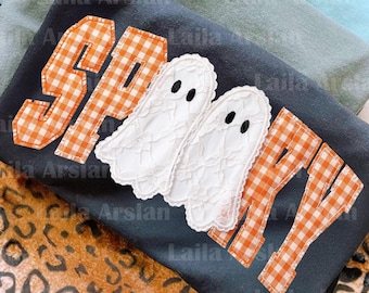 May include: A dark gray t-shirt featuring the word SPOOKY appliqued in orange and white gingham fabric. The two letter O's are replaced by white lace ghost shapes with black embroidered eyes. The shirt is layered over a leopard print fabric.