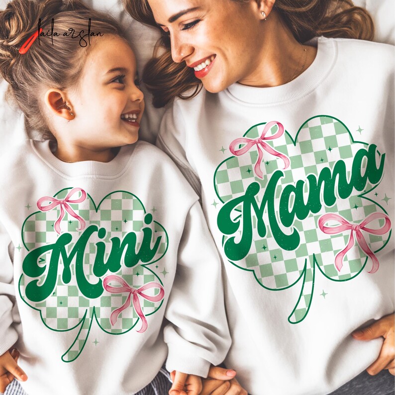 May include: White sweatshirts with green shamrock designs and pink bows. The larger sweatshirt says "Mama" and the smaller sweatshirt says "Mini".