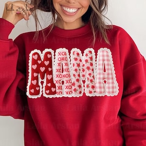 Peut inclure: Sweat-shirt rouge avec le mot "MAMA" en lettres décoratives. Le "M" est rempli de cœurs, le "A" a un motif floral et l'autre "M" est à carreaux. Les lettres sont bordées de dentelle blanche.