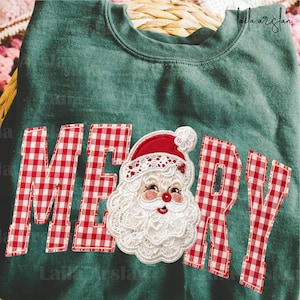 Może przedstawiać: Ciemnozielona bluza z okrągłym dekoltem z napisem MERRY wykonanym z czerwono-białej tkaniny w kratkę. Litera E została zastąpiona szczegółową twarzą Świętego Mikołaja z białej koronki i czerwonego materiału z czerwonym nosem.