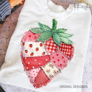 Könnte beinhalten: Weißes Sweatshirt mit einem Erdbeer-Patchwork-Design. Die Erdbeere besteht aus verschiedenen rot- und rosafarbenen Stoffen mit Mustern, darunter Vichy, Herzen und Blumenmuster. Die Erdbeere hat einen grünen Stiel und Blätter. Der Text "ORGINAL DESIGNER" ist sichtbar.
