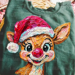 Puede incluir: Una sudadera verde con una ilustración colorida y texturizada de un reno con un gorro de Papá Noel. El reno tiene una nariz roja, ojos grandes y una expresión sonriente. La obra de arte está en un estilo pictórico, con pinceladas visibles.