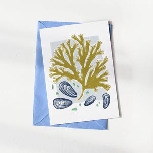 Peut inclure: Carte de vœux avec une illustration botanique d'algues et de moules dans les tons vert olive, bleu marine et vert clair. La carte est sur fond blanc et dans une enveloppe bleu clair.