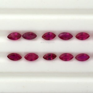 Peut inclure: Dix pierres précieuses en forme de marquise, facettées, de couleur rouge rubis. Les pierres précieuses sont disposées en deux rangées de cinq sur une surface blanche.