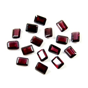 May include: A collection of 16 red gemstone rectangular faceted loose stones. The stones are scattered on a white surface.