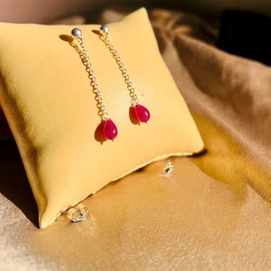 Könnte beinhalten: Ein Paar silberne Ohrringe mit einem rosafarbenen tropfenförmigen Stein am Ende jeder Kette.