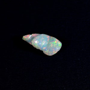 Könnte beinhalten: Ein weißer Opal-Edelstein mit schillernden grünen, blauen und rosa Farbtönen. Der Opal ist muschelförmig und hat eine glatte, polierte Oberfläche.