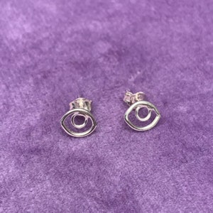 May include: A pair of silver earrings featuring a simple eye design. The earrings are small and delicate, and would make a lovely gift for someone special.