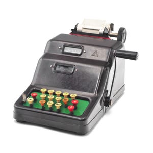 Op de afbeelding: Een vintage zwarte mechanische rekenmachine met een groene basis en kleurrijke cijfertoetsen. De rekenmachine heeft een handvat aan de zijkant en een papieruitvoersleuf. De toetsen zijn geel, oranje en rood, met cijfers en symbolen.